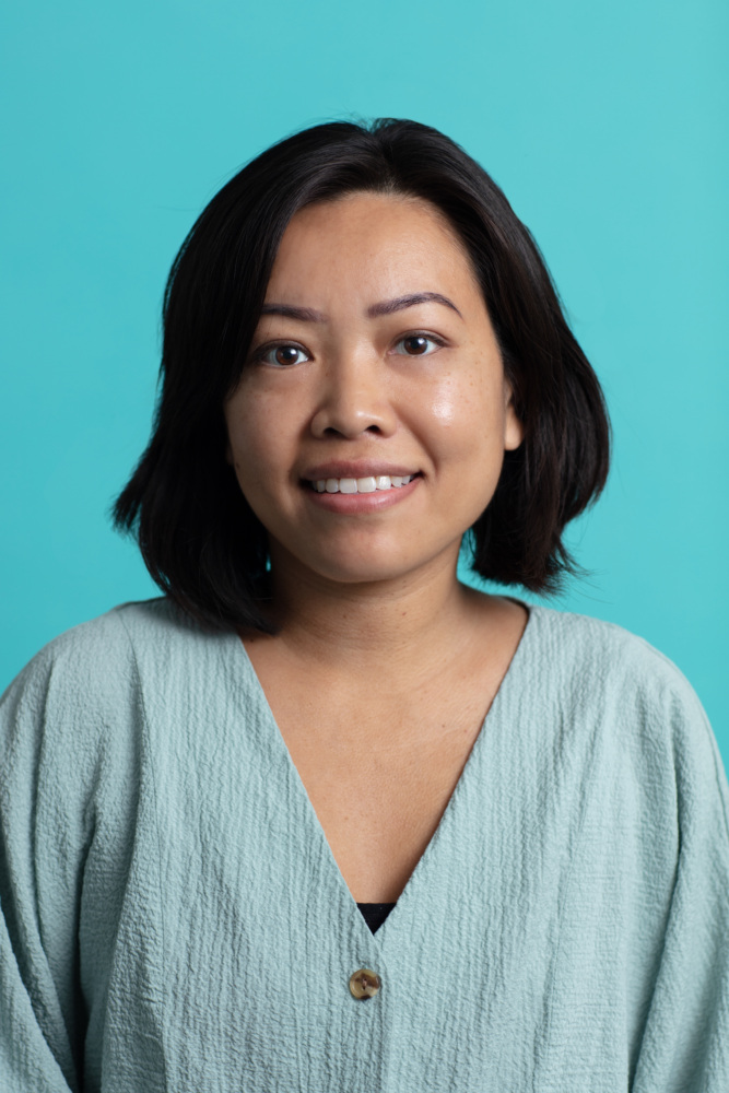 Headshot of Petsamone Thongchanh wearing a light blue blouse with a teal background.